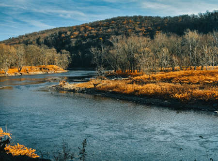 A Large Blue River Flowing Through an Orange Autumn Forest With a Mountain Behind Itの写真素材