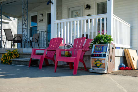 The Front of a Beach House With Two Red Lawn Chairs and a Slot Machine Next to Themの写真素材