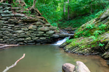 A Long Exposure of a Stream of Water Flowing Into a Small Body of Water Next to a Cobblestone Wallの写真素材
