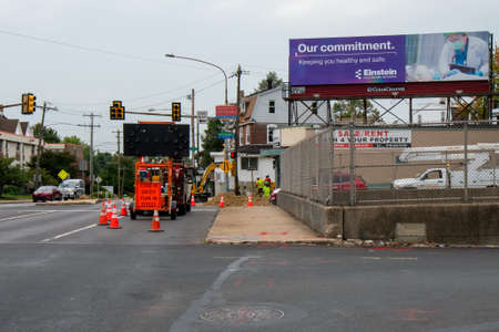 ELKINS PARK, PA - SEPTEMBER 24, 2020: Construction Workers at Work on the Side of the Road With a Sign That States a COVID-19 Safety Plan is in Effect.のeditorial素材
