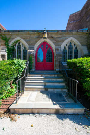 Steps Leading Up to a Red Door on a Cobblestone Church With Trimmed Bushes On Each Sideの写真素材
