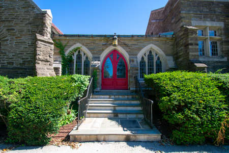 Steps Leading Up to a Red Door on a Cobblestone Church With Trimmed Bushes On Each Sideの写真素材