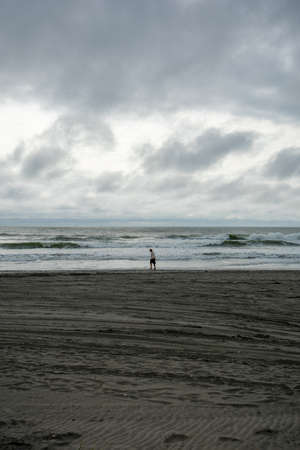 A Lonely Man Walking Across the Beach With a Dramatic Stormy Sky Over the Horizonの写真素材