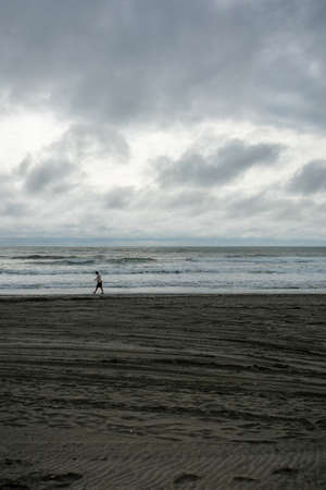 A Lonely Man Walking Across the Beach With a Dramatic Stormy Sky Over the Horizonの写真素材