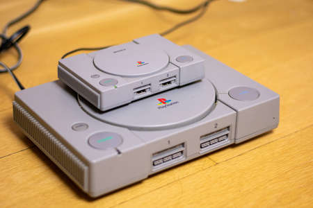A Playstion Classic On Top of an Original Playstation, a comparison of the two, on a wood floor.のeditorial素材