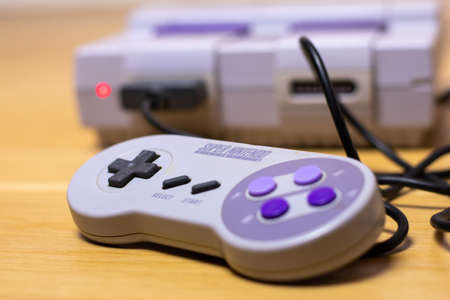 The Controller of a Super Nintendo Entertainment System plugged into the Popular Retro Console on a wood floor.のeditorial素材