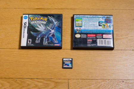 A Pokemon Diamond Cartridge and The Front and Back of It's Game Case for the Nintendo DS on a wood floor.のeditorial素材