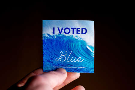 November 3, 2020 - Elkins Park, Pennsylvania: An Election Day Sticker Held by a Hand That Says I Voted Blue With a Wave in the Background on Blackのeditorial素材