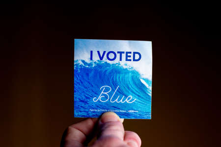 November 3, 2020 - Elkins Park, Pennsylvania: An Election Day Sticker Held by a Hand That Says I Voted Blue With a Wave in the Background on Blackのeditorial素材
