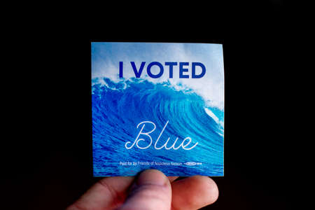 November 3, 2020 - Elkins Park, Pennsylvania: An Election Day Sticker Held by a Hand That Says I Voted Blue With a Wave in the Background on Blackのeditorial素材