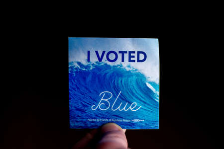 November 3, 2020 - Elkins Park, Pennsylvania: An Election Day Sticker Held by a Hand That Says I Voted Blue With a Wave in the Background on Blackのeditorial素材