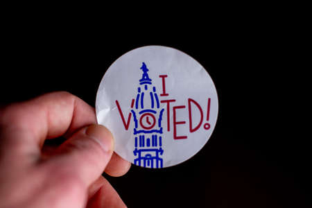 November 3, 2020 - Elkins Park, Pennsylvania: An Election Day Sticker Held by a Hand That Says I Voted Blue With a Wave in the Background on Blackのeditorial素材
