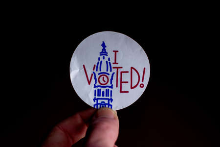November 3, 2020 - Elkins Park, Pennsylvania: An Election Day Sticker Held by a Hand That Says I Voted Blue With a Wave in the Background on Blackのeditorial素材