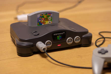 A Nintendo 64 Console With the Power Indicator Light On and Super Mario 64 in the Cartridge Slot and a Controller Plugged Into Itのeditorial素材