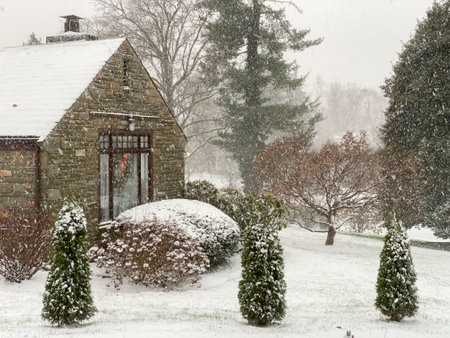 A Cobblestone Home With a Wreath in a Window next to a Suburban Street During a Snowstormの写真素材