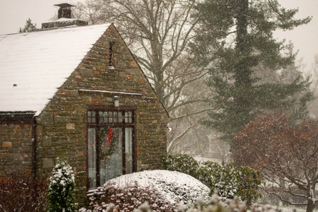 A Cobblestone Home With a Wreath in a Window next to a Suburban Street During a Snowstormの写真素材