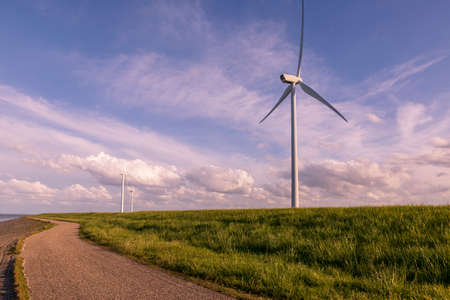 Road on coast near sea and wind electric mill. The background is a nice blue sky with white clouds...