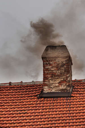 Red roof with a chimney and dark smoke coming from the chimney.の写真素材