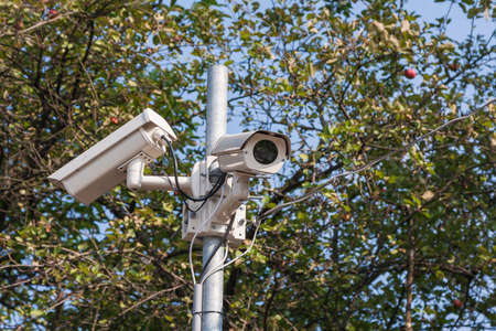 Security cameras to capture the surrounding area. Background are green trees and blue sky.