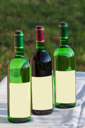Three wine bottles - red and white standing on white mat. Background is natural green. Label without labeling.の写真素材