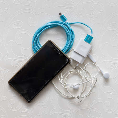 Flatlay phone, charger, headphones on white tableの写真素材