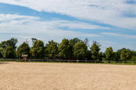 Fence for horses where races are held. There is sand on the ground, trees and blue sky with white clouds on the background.の写真素材