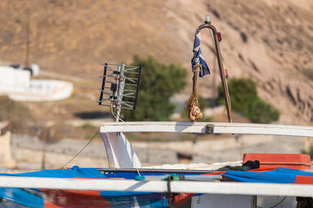 A television antenna mounted on a boat by the sea and a net with garlic that is being dried.