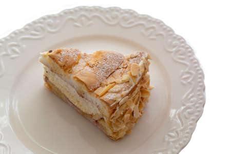 Sponge cake with cream sprinkled with nuts on a white plate and background.の写真素材