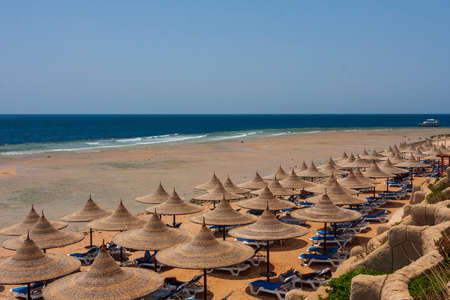View of the sandy beach on which there are natural umbrellas, sunbeds. In the background is the sea and pontoons to enter the sea. Send backの写真素材