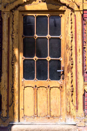 Old brown peeling door. There are black panels on the door. The sun is shining on the door.の写真素材