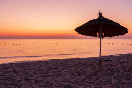 Sunrise on the beach with parasol overlooking the sea and the sun in Tunisia.の写真素材