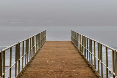 Metal pier leading to the surface of the drained dam. There is fog in the background.