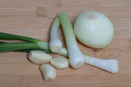 Spring green onions, garlic and onions on a brown wooden kitchen board.の写真素材