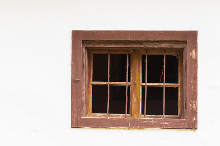 Window with a wooden frame on a white wall of the house. There is a grille in the windows. There are...