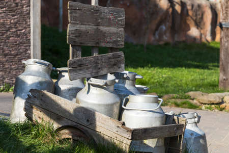 Old metal milk jugs on a wooden cart by the road.の写真素材