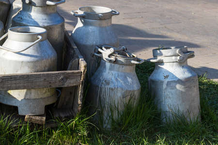 Old metal milk jugs on a wooden cart by the road.