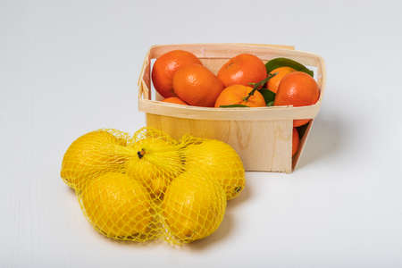 Citrus fruits. Lemons in a net and tangerines in a basket for sale. The background is white.の写真素材