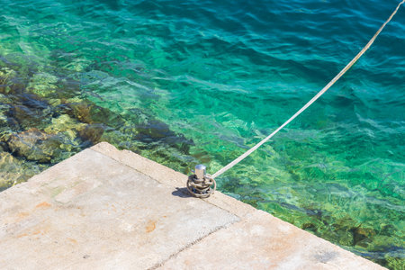 A concrete pier by the sea with a metal pin for anchoring a boat.
