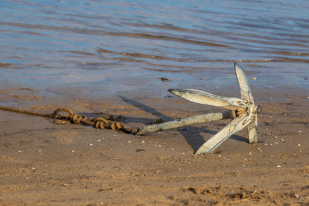 A small iron anchor is in the sand on the beach by the sea.
