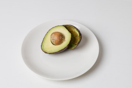 Avocado cut in half on a white plate. A seed in an avocado.
