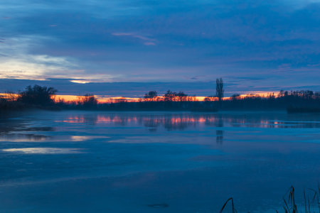 Winter landscape of a frozen pond. Blue hour after sunset. Beautiful clouds and frozen pond surface.の写真素材