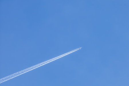 A large airliner in a cloudless blue sky. There is a long trail behind the plane.の写真素材