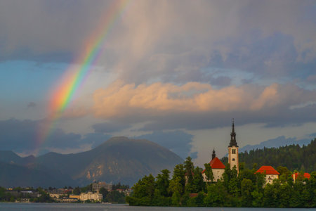 Church of the Assumption of the Blessed Virgin Mary on an island on Lake Bled in Slovenia. There is a dramatic sky in the sky with a colorful rainbow.の写真素材