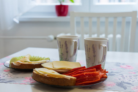 Breakfast on the kitchen table. Bread with salami and cheese. Garnish is vegetables - cucumber and...