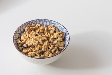 A detailed, studio-style shot of a bowl filled with shelled walnut kernels. The nutrient-rich nuts...