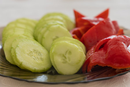 A close-up, top-down view of a plate containing sliced cucumber pieces and chunks of red bell pepper, divided into two distinct color sections.の写真素材