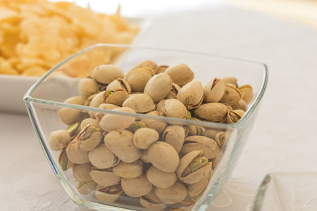 This close-up shot captures a square glass bowl brimming with roasted and salted in-shell...