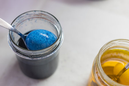 A close-up of the process of dyeing an Easter egg. The egg is being removed from the dye in a jar with a spoon. Other jars of dye are visible in the background.の写真素材