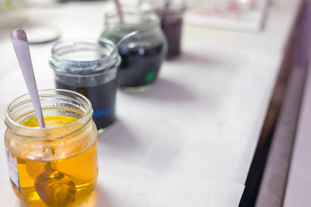 A close-up of a glass container of water into which egg dye is being poured or dissolved. The concentrated dye is visible at the bottom of the container, dissolving in the water.の写真素材