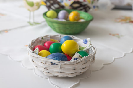 A small woven basket full of brightly colored Easter eggs in blue, yellow, green and red. The basket...